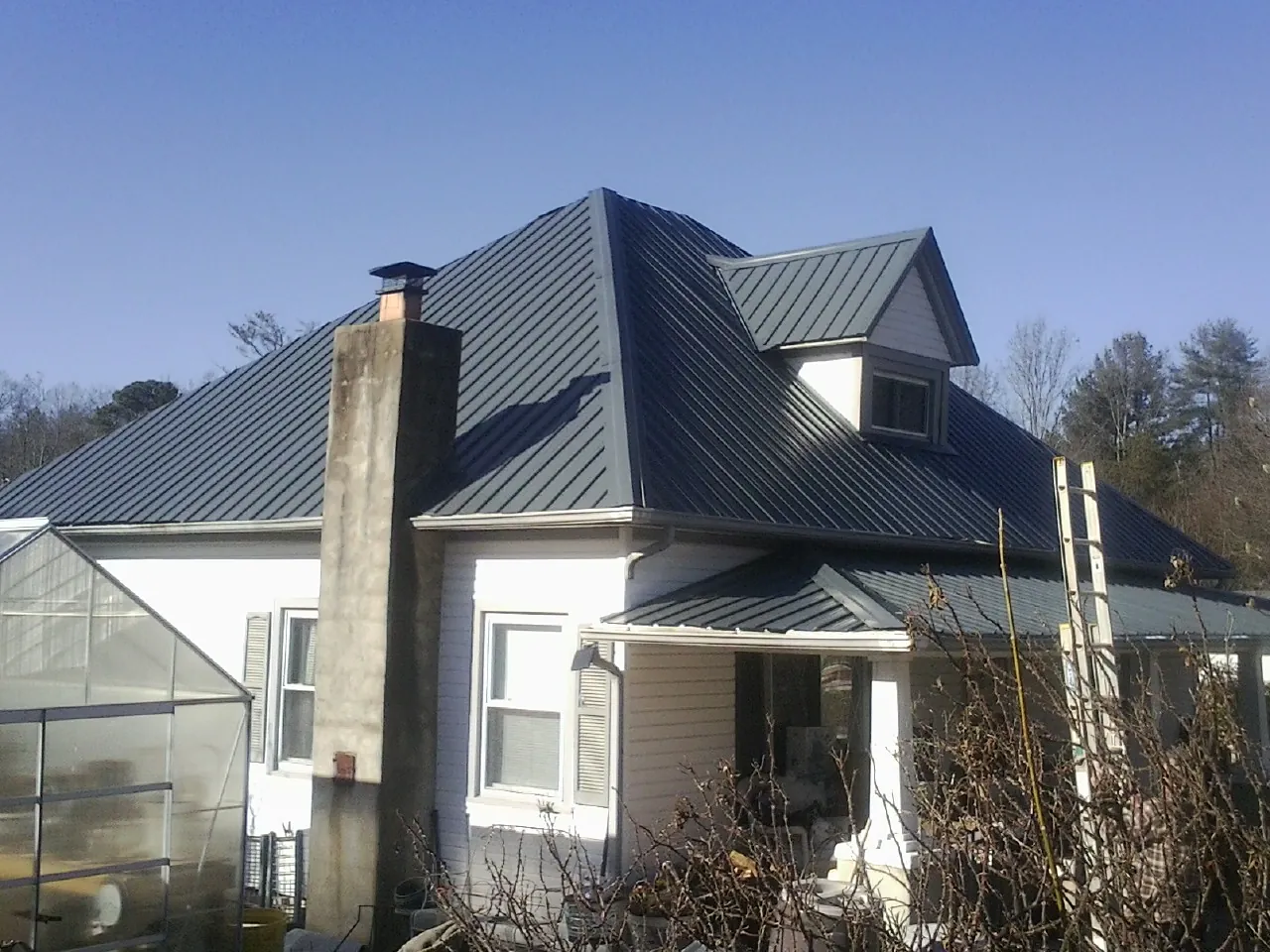 Dark blue standing seam metal roof on a white farmhouse with dormer — Slate & Tile Roof Repair by Roofing Brothers in Milligan