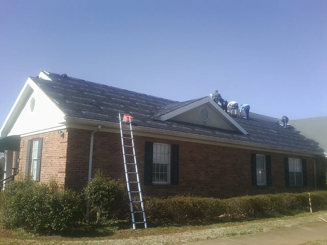Crew tearing shingles off a brick ranch roof with a ladder set — Emergency Roof Repair work by our crew in Milligan
