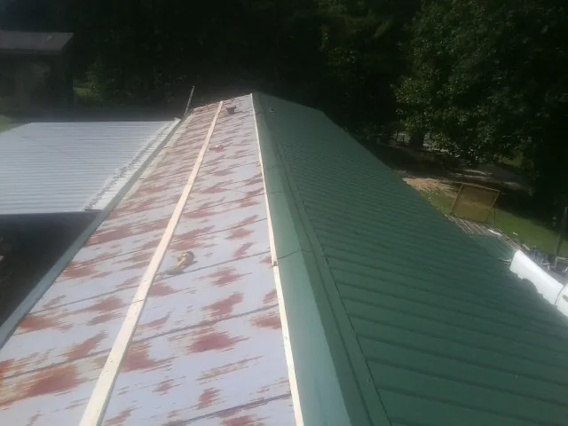 Old rusted panels beside newly installed green metal roofing — Wind Damage Roof Repair by Roofing Brothers in Milligan