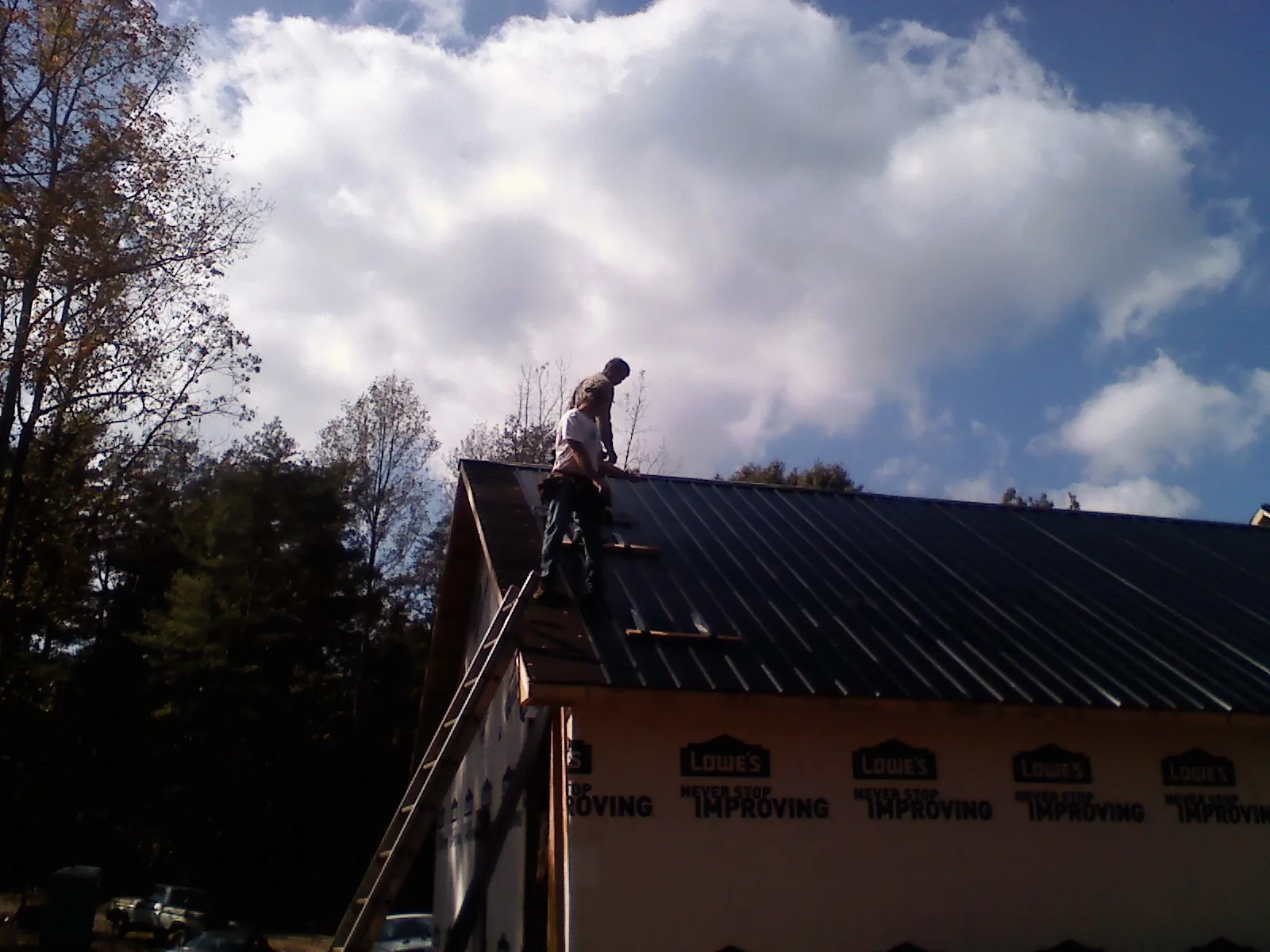 Roofer fastening dark metal panels high against a cloudy sky, from a Roof Inspection job in Milligan